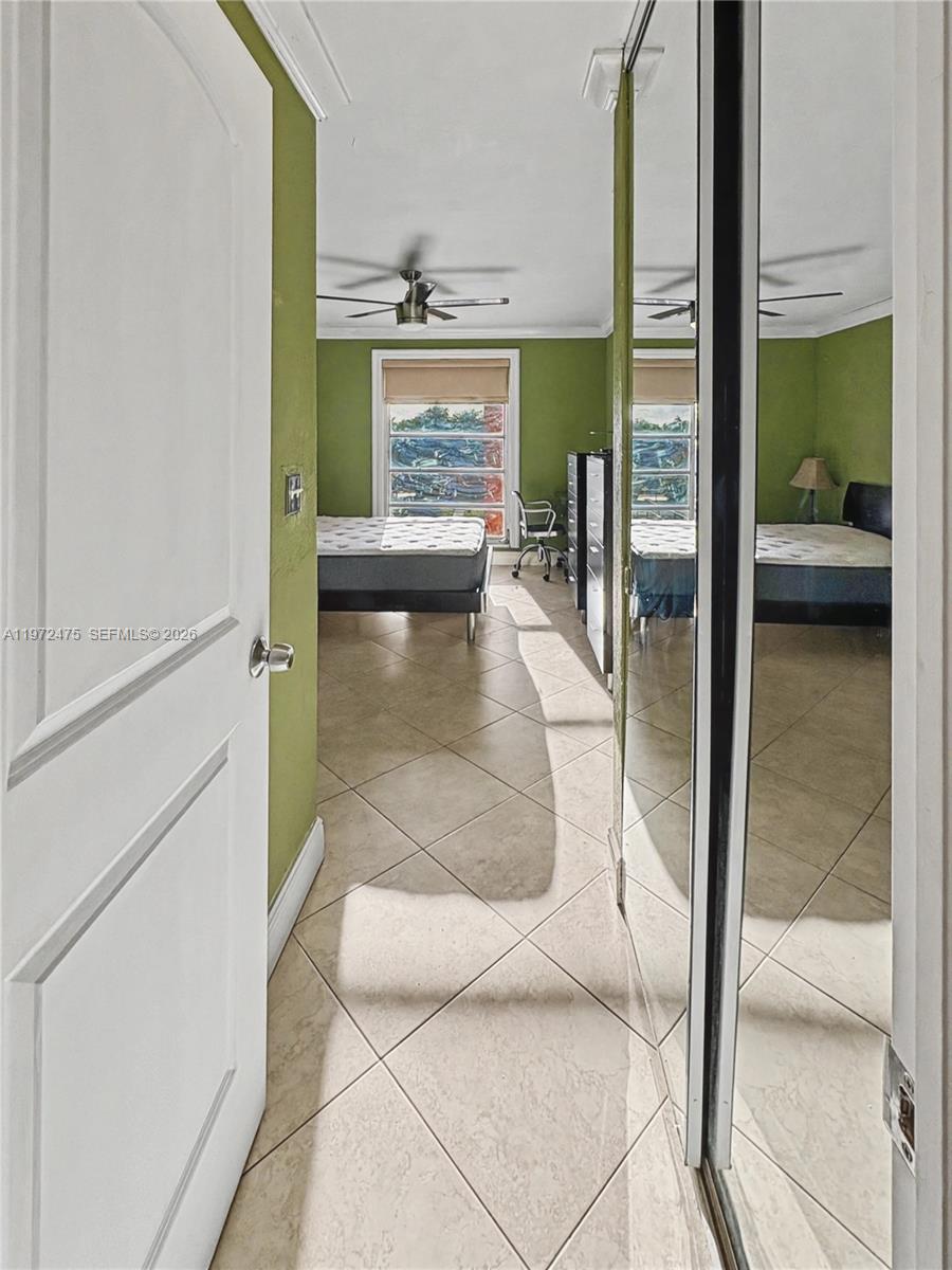 A bedroom with green walls, tile flooring, and mirrored closet doors is viewed through a doorway — 9417 SW 76th St # X36, Miami FL 33173, MIAMI, FL