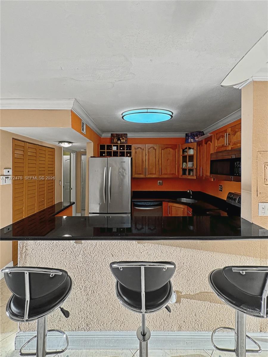 A kitchen features wood cabinets, black countertops, stainless steel appliances, and three bar stools — 9417 SW 76th St # X36, Miami FL 33173, MIAMI, FL