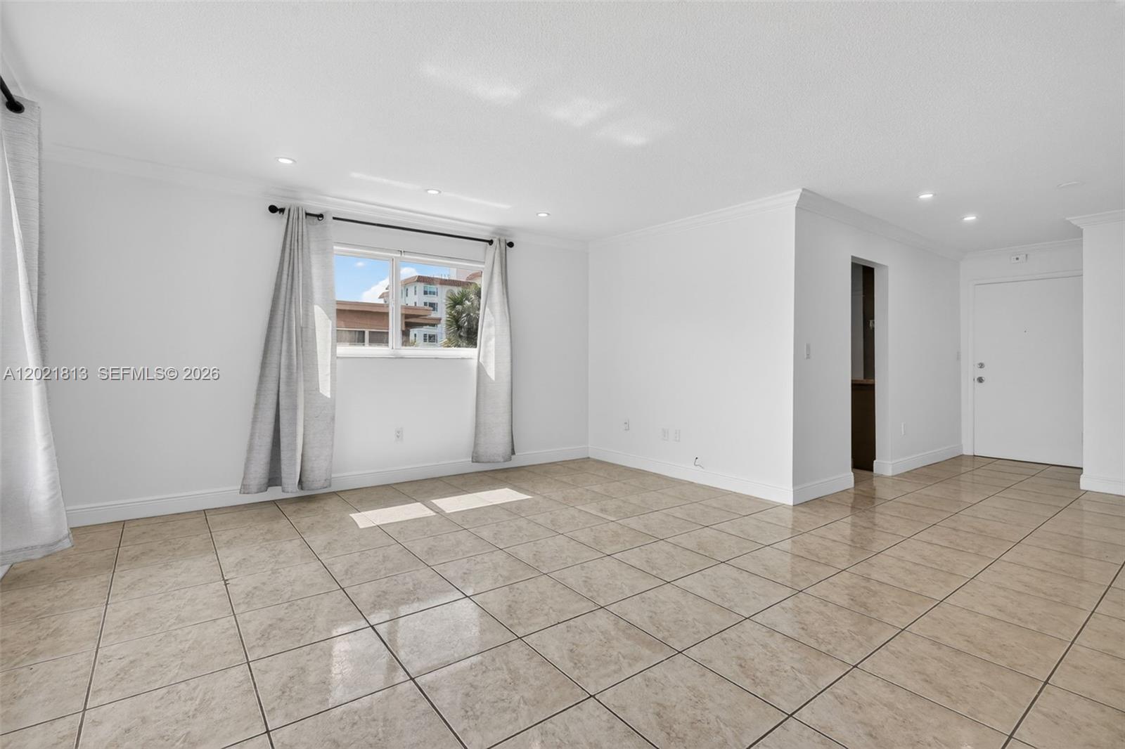 An empty room features white walls, beige tile flooring, a window with curtains, and recessed lighting — 1020 94th St # 301, Bay Harbor Islands FL 33154, BAY HARBOR ISLANDS, FL