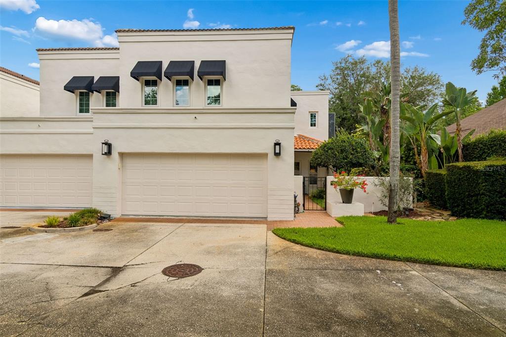 A two-story stucco townhouse features a two-car garage, black window awnings, and a gated entrance — 3133 LAKE ELLEN DRIVE, TAMPA, FL