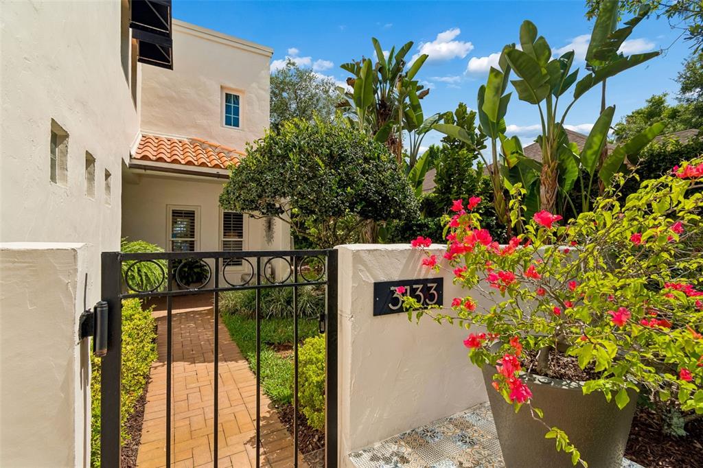 A wrought iron gate opens to a brick walkway leading to a stucco house entrance — 3133 LAKE ELLEN DRIVE, TAMPA, FL
