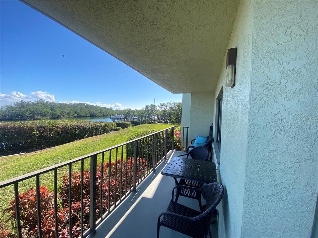 A covered balcony features a metal table and chairs overlooking a grassy lawn and water — 1515 PINELLAS BAYWAY S UNIT 1, ST PETERSBURG, FL