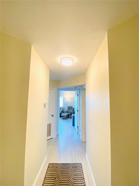 A hallway with light-colored walls and flooring leads toward a room with a recliner chair — 1515 PINELLAS BAYWAY S UNIT 1, ST PETERSBURG, FL