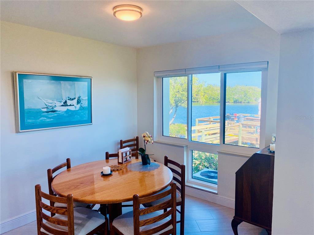 A dining area with a wooden table, chairs, and a window overlooking a waterfront dock — 1515 PINELLAS BAYWAY S UNIT 1, ST PETERSBURG, FL