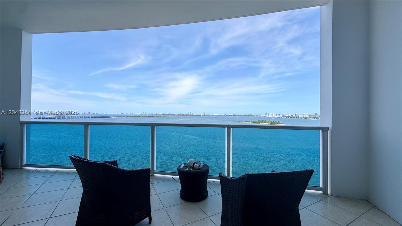 A balcony with two wicker chairs and a small table overlooks a large bay — 725 NE 22nd St # 14E, Miami FL 33137, MIAMI, FL