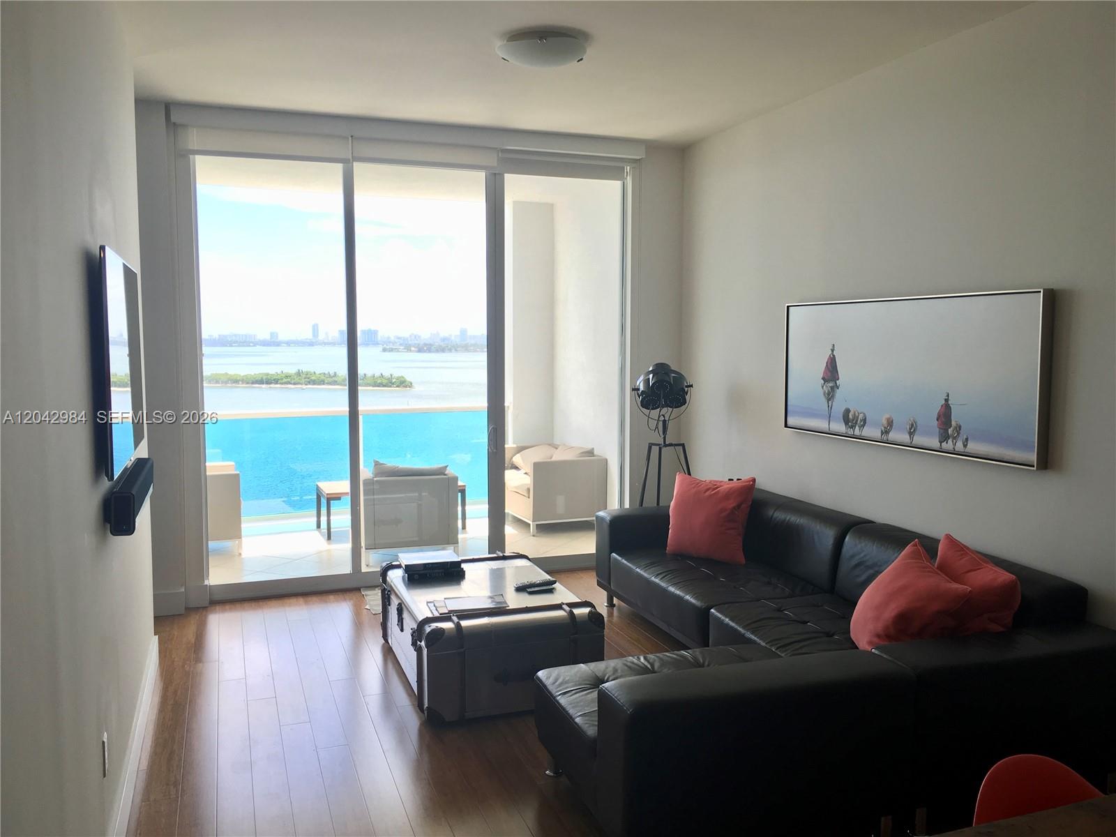A living room features a black leather sectional, a trunk coffee table, and a balcony view — 725 NE 22nd St # 14E, Miami FL 33137, MIAMI, FL