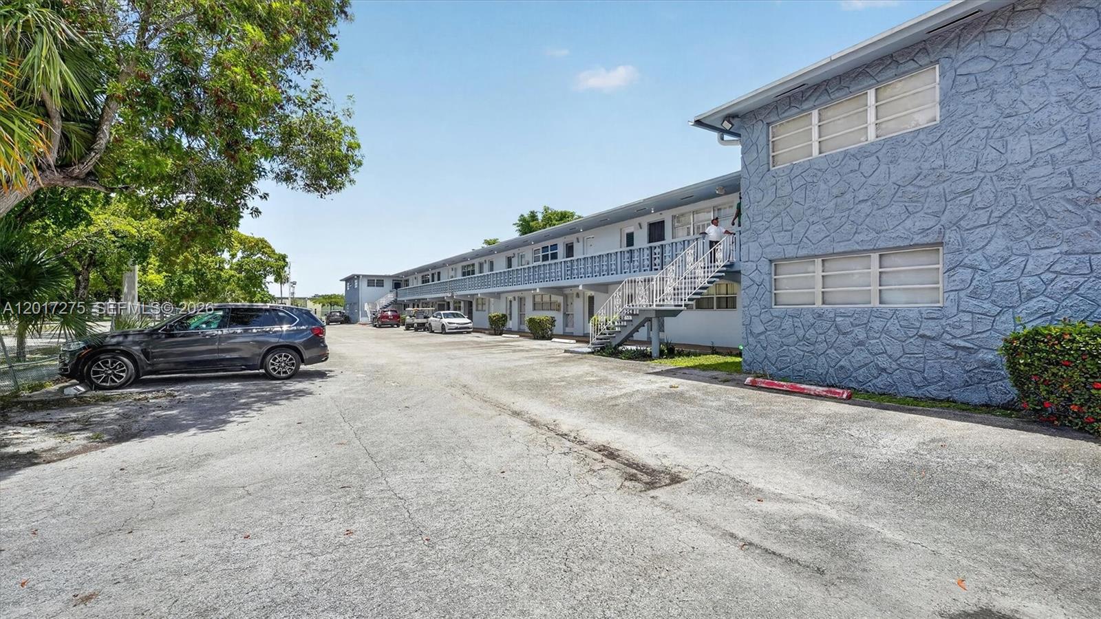A two-story apartment building with a blue stone facade features an exterior staircase and parking — 300 NE 191st St # 219, Miami FL 33179, MIAMI, FL