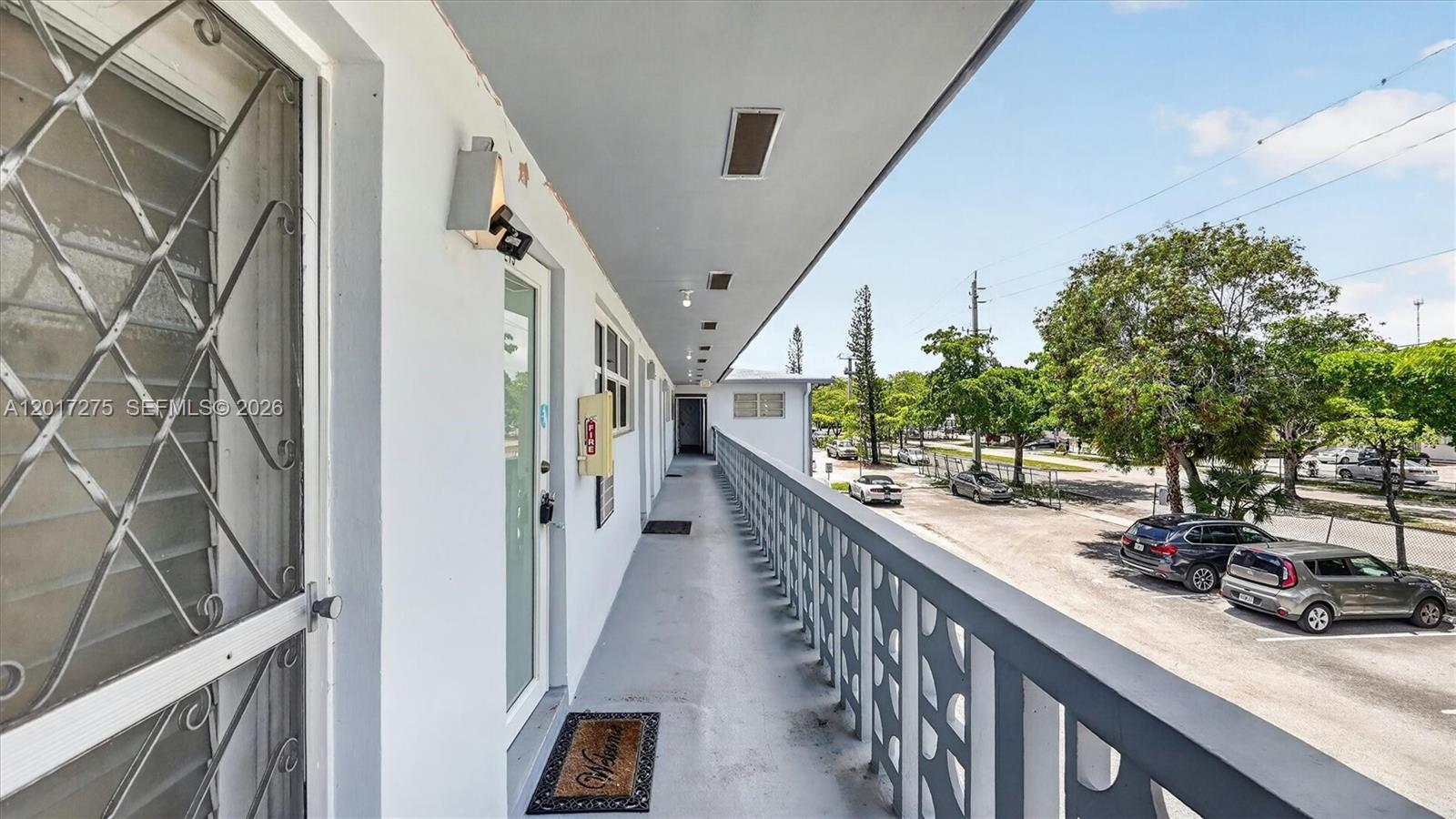 An exterior walkway with a metal railing overlooks a parking lot with several cars — 300 NE 191st St # 219, Miami FL 33179, MIAMI, FL