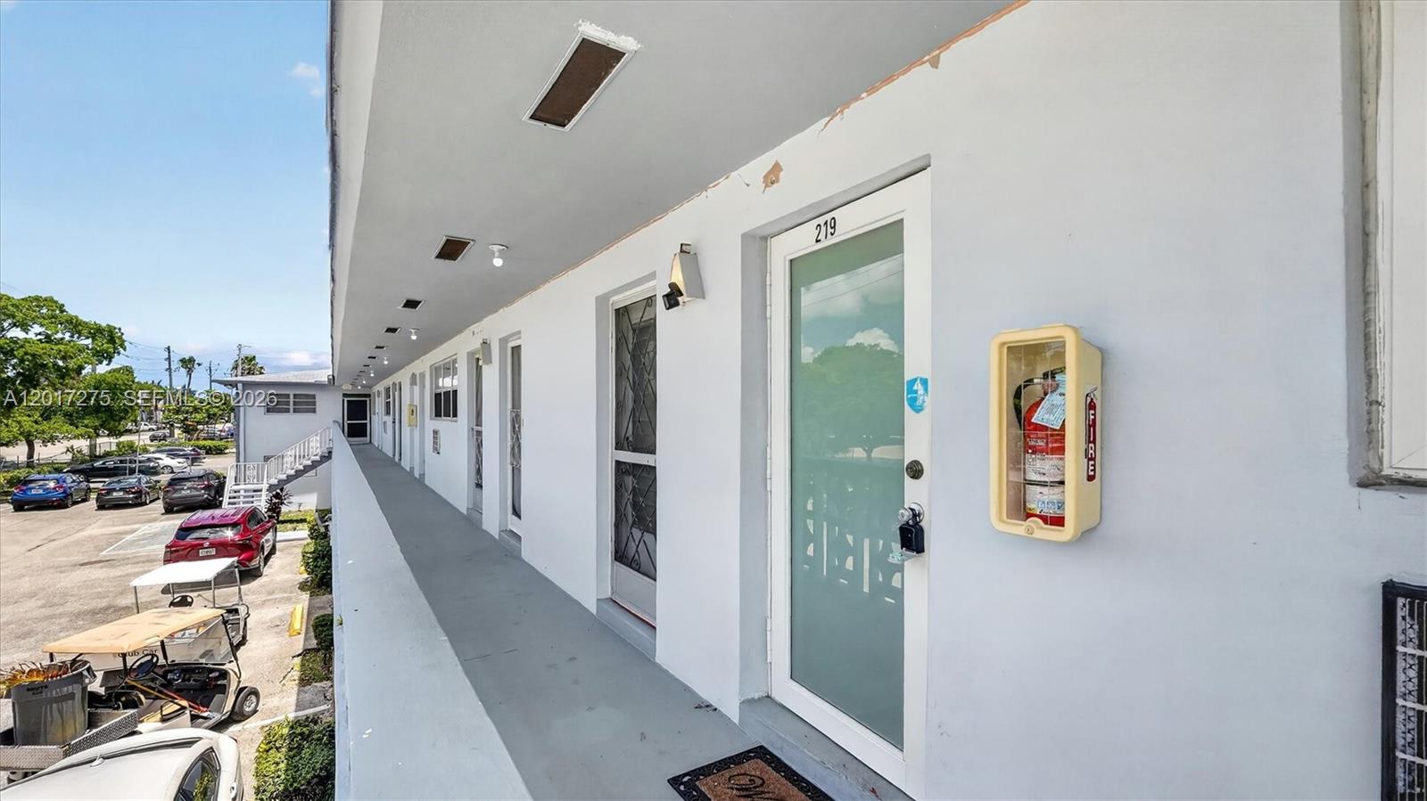 An exterior walkway leads past several apartment doors with a fire extinguisher mounted on the wall — 300 NE 191st St # 219, Miami FL 33179, MIAMI, FL