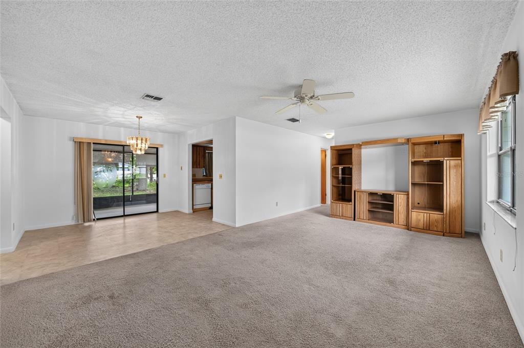A living and dining area with beige carpet, tile flooring, and a large wooden entertainment center — 610 FOURTH AVENUE, LADY LAKE, FL