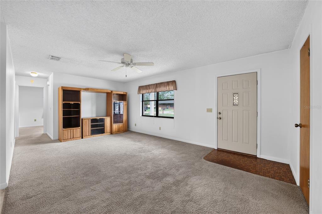 A living room with beige carpet, a wooden entertainment center, and a front entry door — 610 FOURTH AVENUE, LADY LAKE, FL