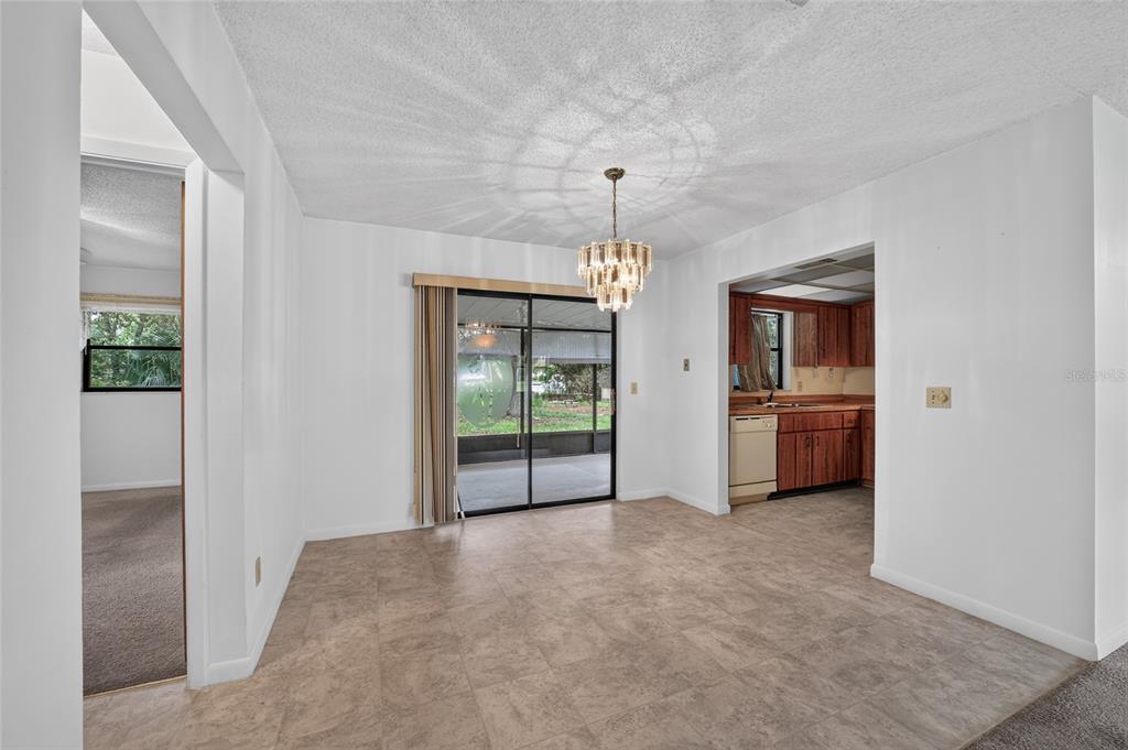 A dining area with tile flooring, a chandelier, sliding glass doors, and an adjacent kitchen — 610 FOURTH AVENUE, LADY LAKE, FL