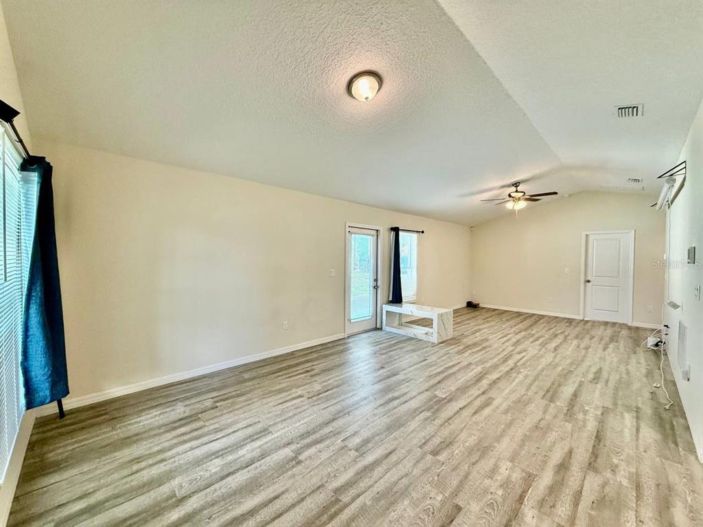 An empty living room features light wood-look flooring, a ceiling fan, and a glass door — 2904 E COLUMBUS DRIVE, TAMPA, FL