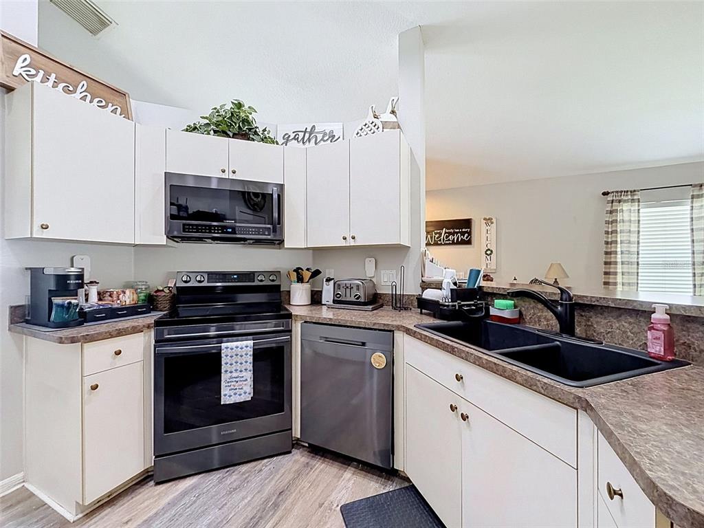 A kitchen features white cabinets, dark countertops, stainless steel appliances, and a black sink — 11627 LEDA LANE, NEW PORT RICHEY, FL