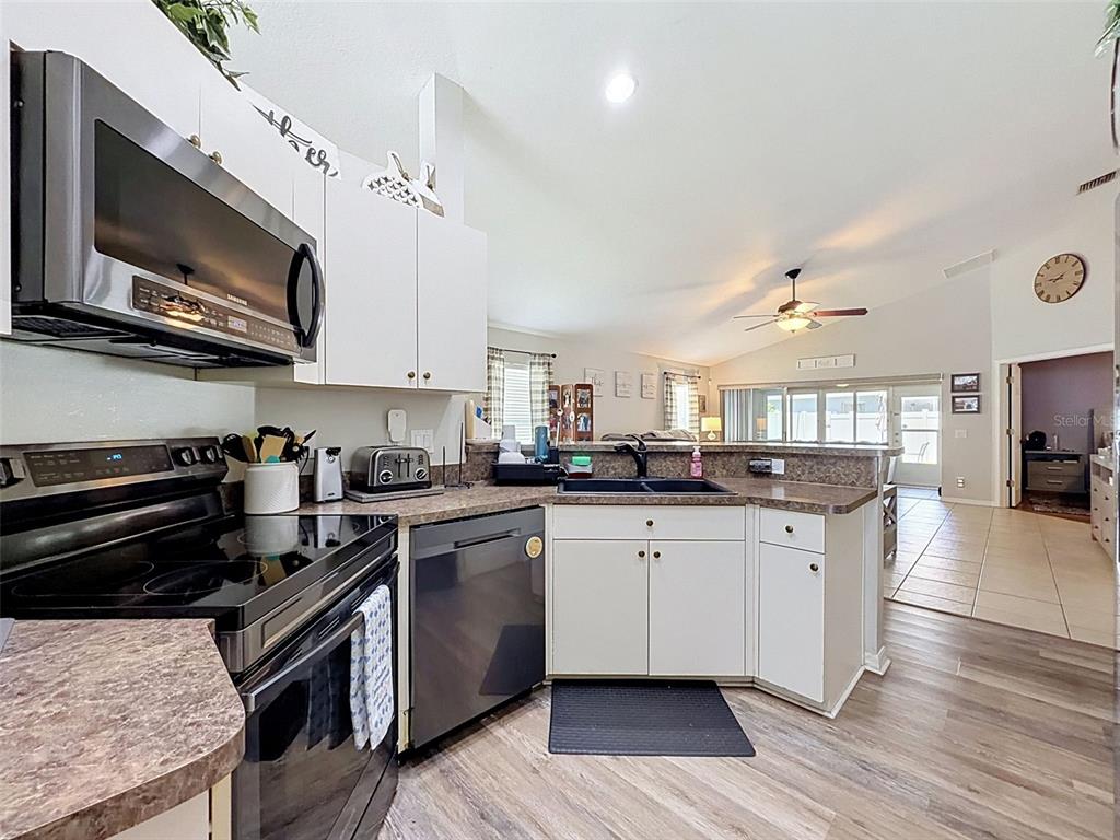 A kitchen with white cabinets, dark appliances, and a laminate countertop overlooks an open living area — 11627 LEDA LANE, NEW PORT RICHEY, FL