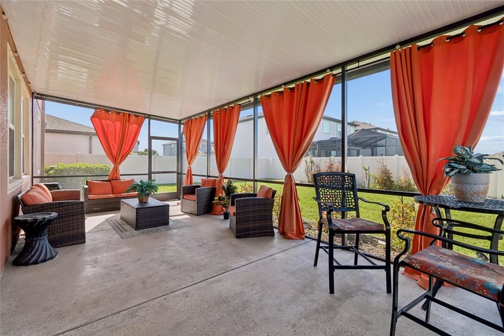 A screened-in patio features concrete flooring, wicker furniture, and orange curtains overlooking a backyard — 11804 BLUEGRASS FIELD COURT, RIVERVIEW, FL