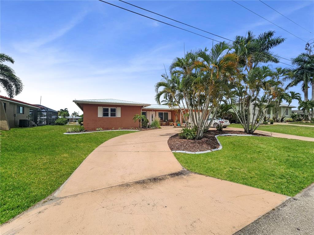 A single-story house with a terracotta-colored exterior and a curved driveway sits behind palm trees — 270 BELAIRE COURT, PUNTA GORDA, FL
