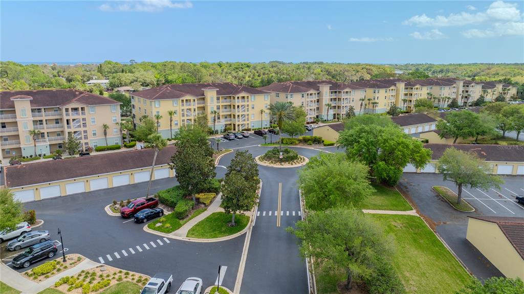 An aerial view shows multi-story apartment buildings, parking lots, and landscaped grounds under a blue sky — 400 CANOPY WALK LN UNIT 425, PALM COAST, FL
