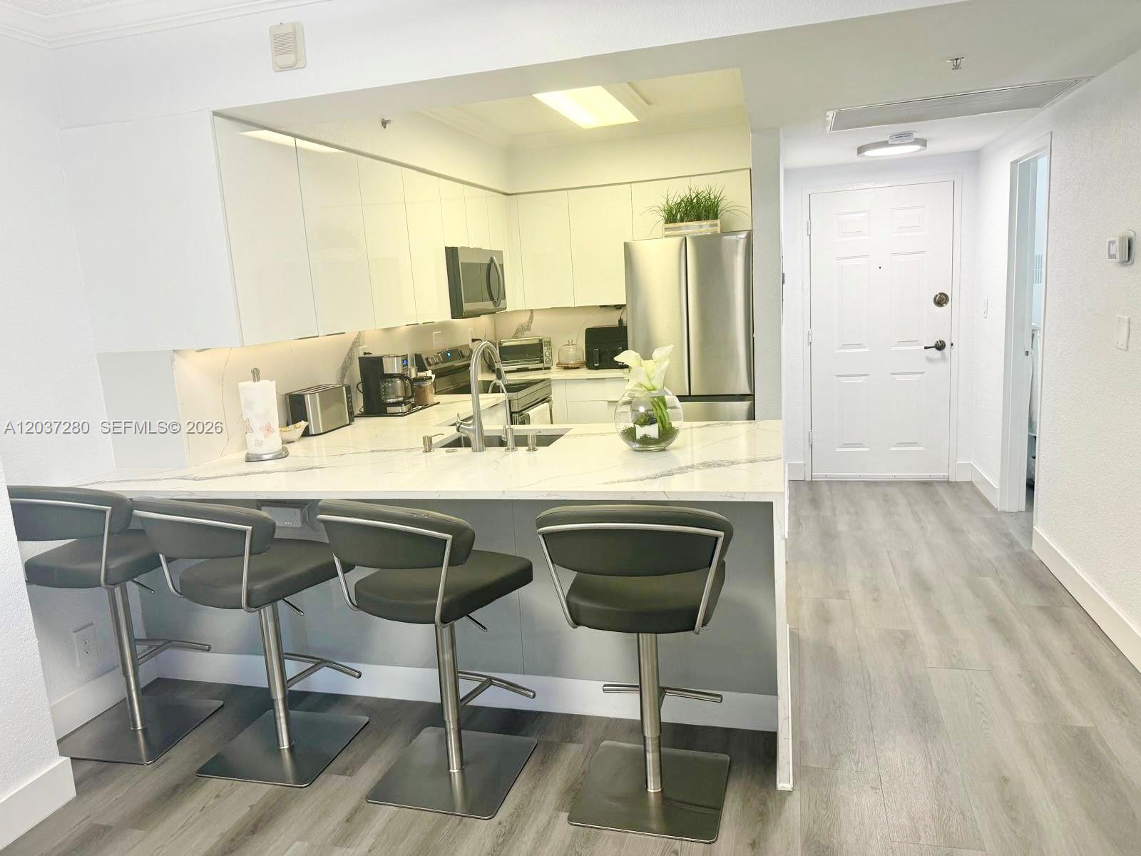 A modern kitchen features white cabinetry, a marble-topped breakfast bar, and four gray barstools — 2501 S Ocean Dr # L14, Hollywood FL 33019, HOLLYWOOD, FL
