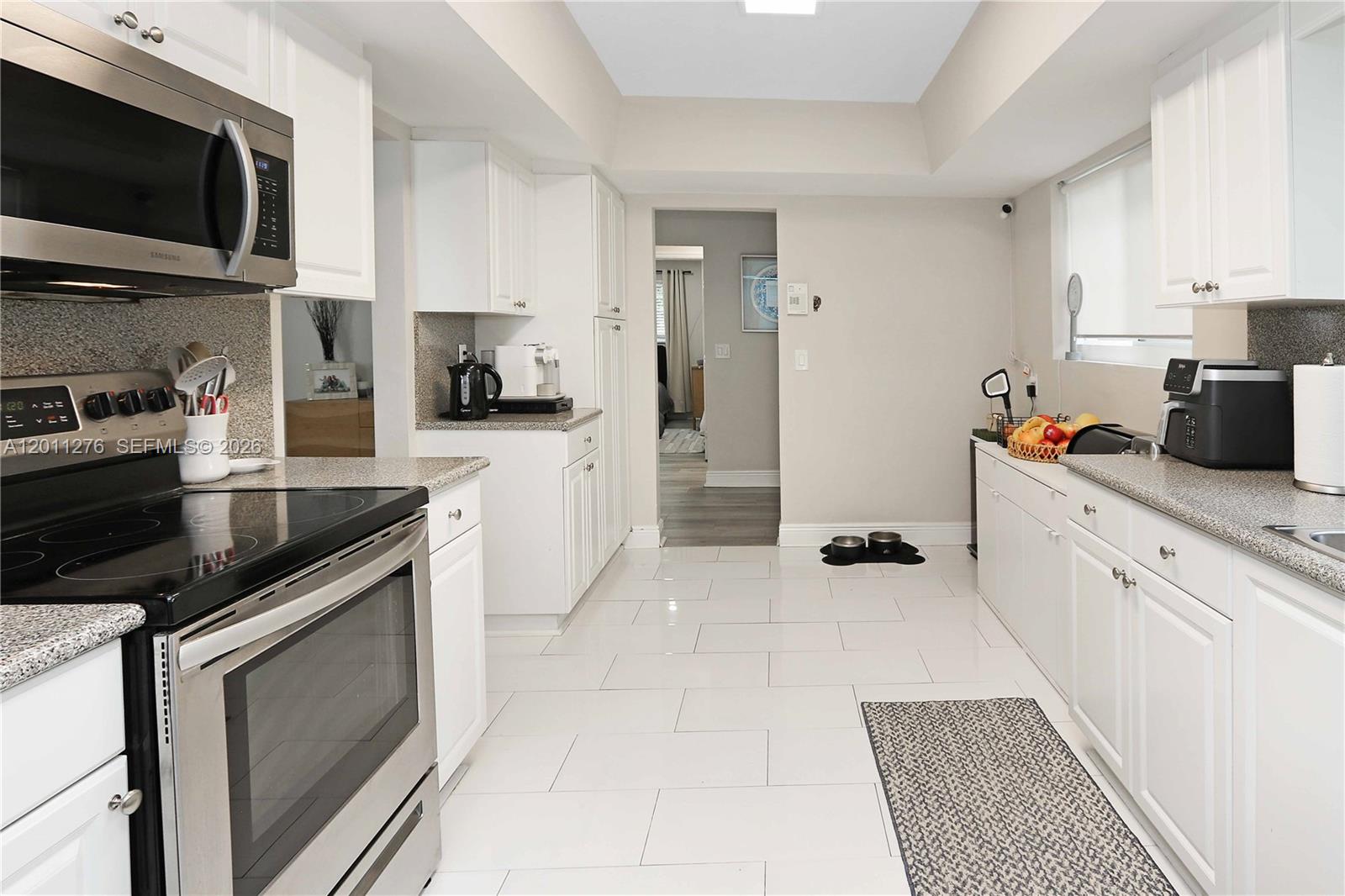 A galley kitchen features white cabinets, granite countertops, stainless steel appliances, and white tile flooring — 1333 Tyler St, Hollywood FL 33019, HOLLYWOOD, FL