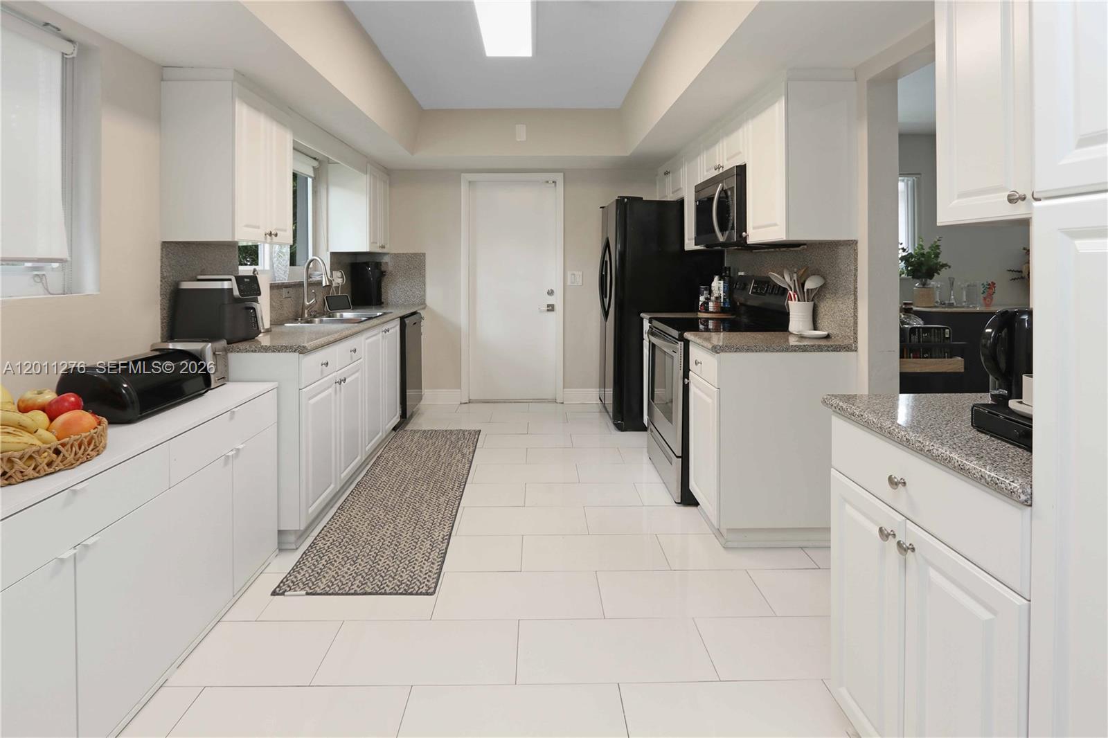 A white kitchen features granite countertops, black appliances, and light-colored tile flooring — 1333 Tyler St, Hollywood FL 33019, HOLLYWOOD, FL