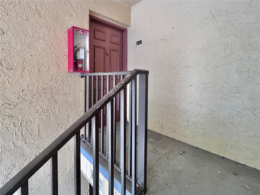 A red door marked B12 is accessed by a staircase with a black metal railing — 4455 38TH TERRACE N UNIT B12, ST PETERSBURG, FL