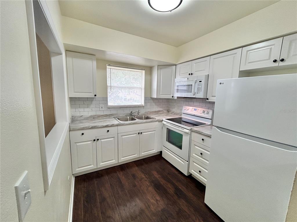 A kitchen featuring white cabinets, a white refrigerator, a white stove, and wood-look flooring — 4455 38TH TERRACE N UNIT B12, ST PETERSBURG, FL
