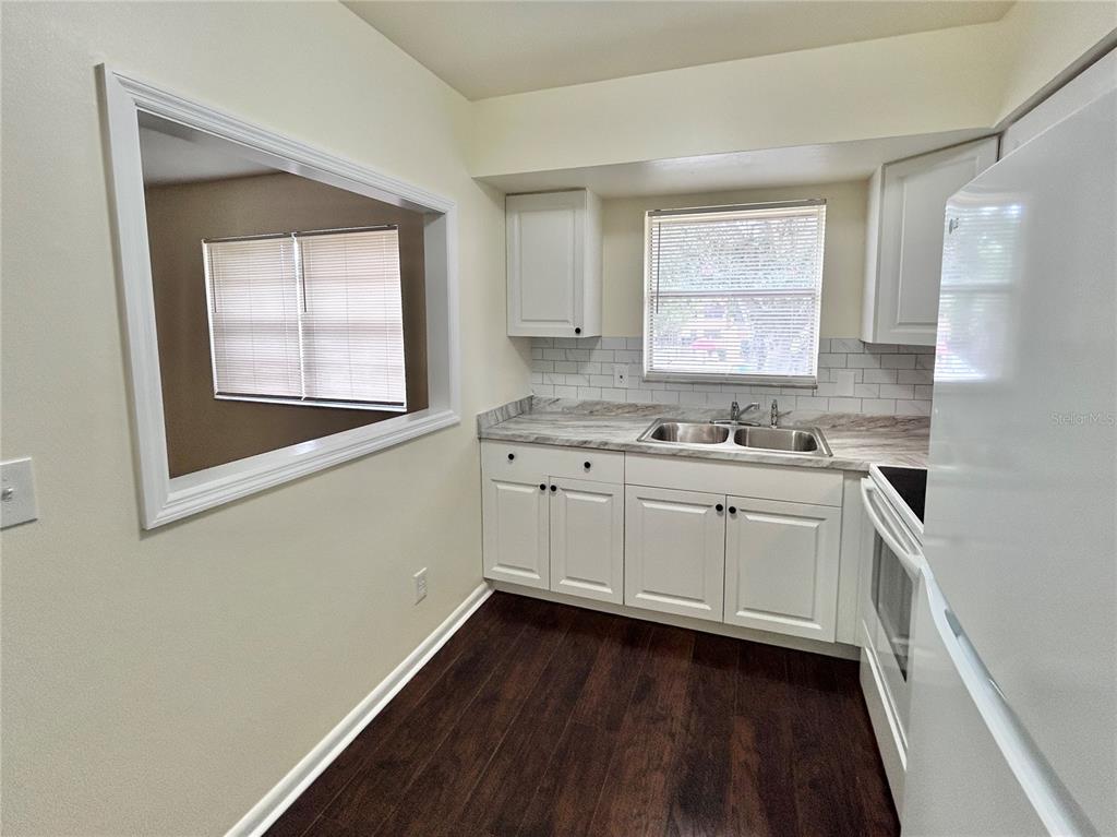 A kitchen features white cabinets, a double sink, a window, and dark wood-look flooring — 4455 38TH TERRACE N UNIT B12, ST PETERSBURG, FL