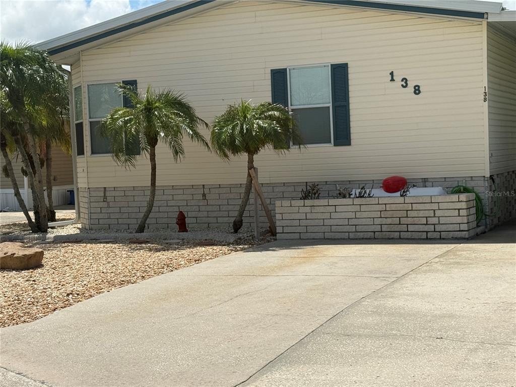 A single-story mobile home with beige siding, a concrete driveway, and small palm trees — 138 S SAINT THOMAS CIRCLE, APOLLO BEACH, FL