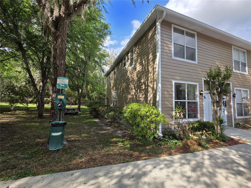 A two-story tan siding townhouse exterior features a pet waste station and a wooded area — 4415 SW 34TH ST UNIT 410, GAINESVILLE, FL