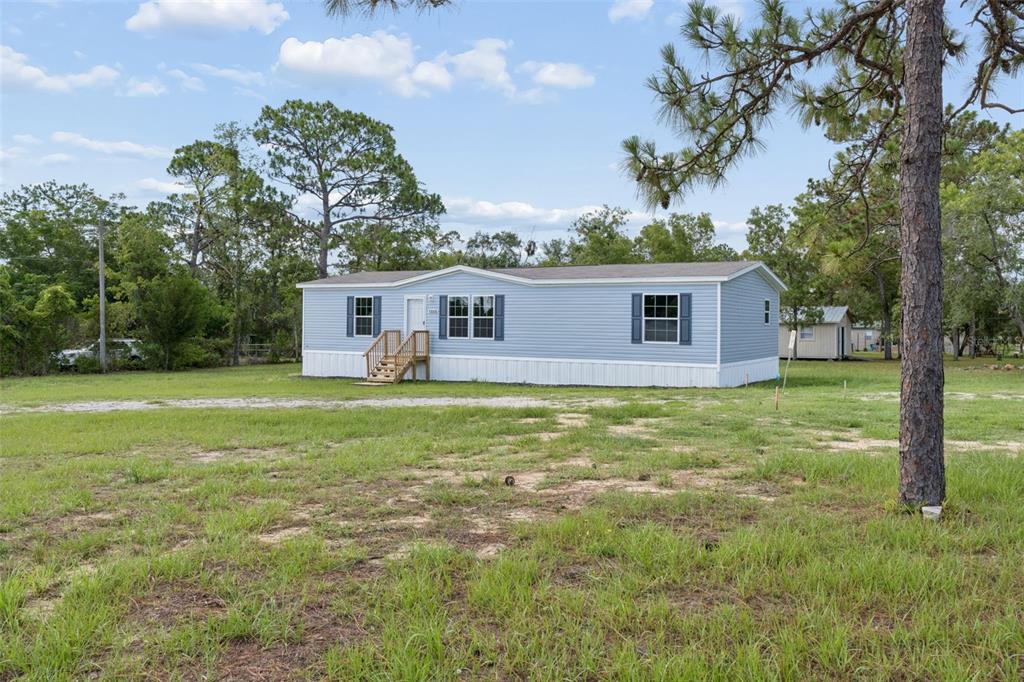 A light blue manufactured home sits on a grassy lot surrounded by pine trees — 13320 SUN ROAD, BROOKSVILLE, FL