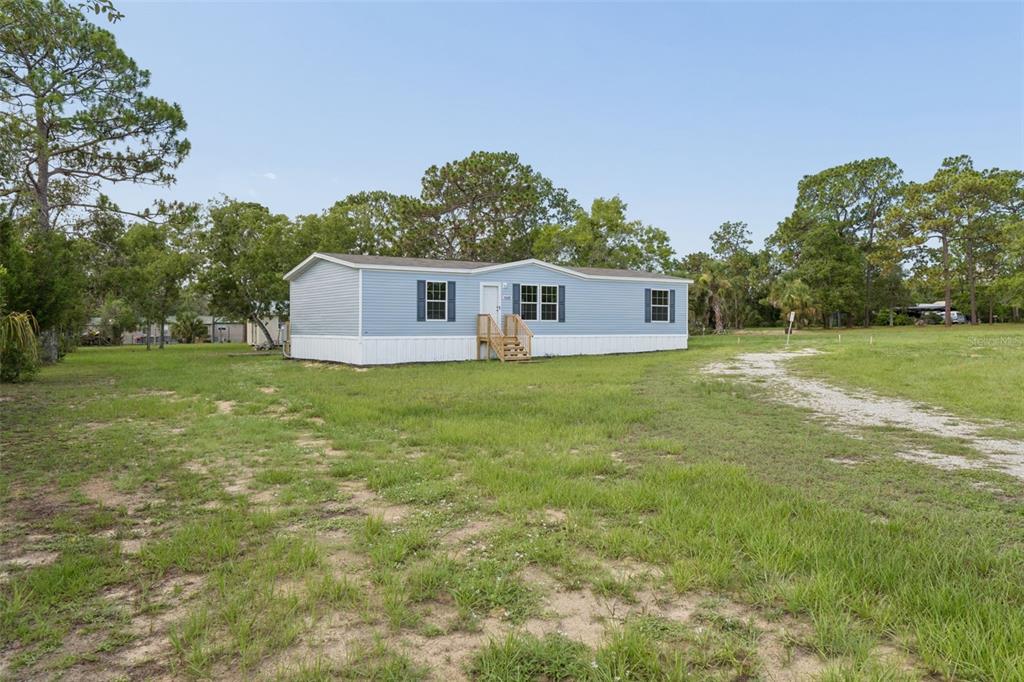A light blue manufactured home sits on a grassy lot surrounded by pine trees — 13320 SUN ROAD, BROOKSVILLE, FL