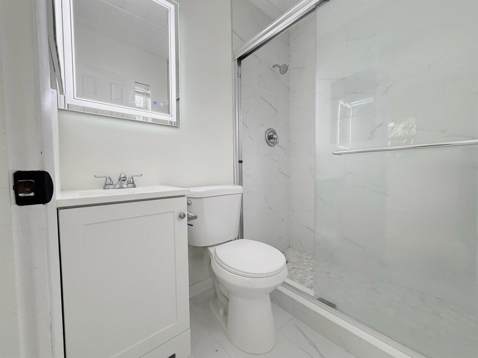 A modern bathroom features a white vanity, a toilet, and a glass-enclosed marble-tiled shower — 1713 Florida Avenue Unit B4, West Palm Beach FL 33401, WEST PALM BEACH, FL