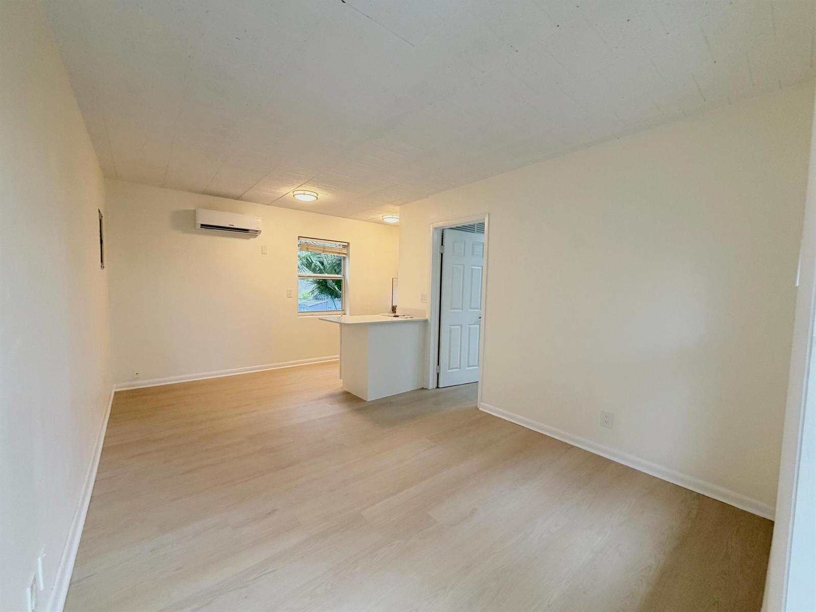An empty room with light wood-look flooring, white walls, a window, and a kitchen counter — 1713 Florida Avenue Unit B4, West Palm Beach FL 33401, WEST PALM BEACH, FL