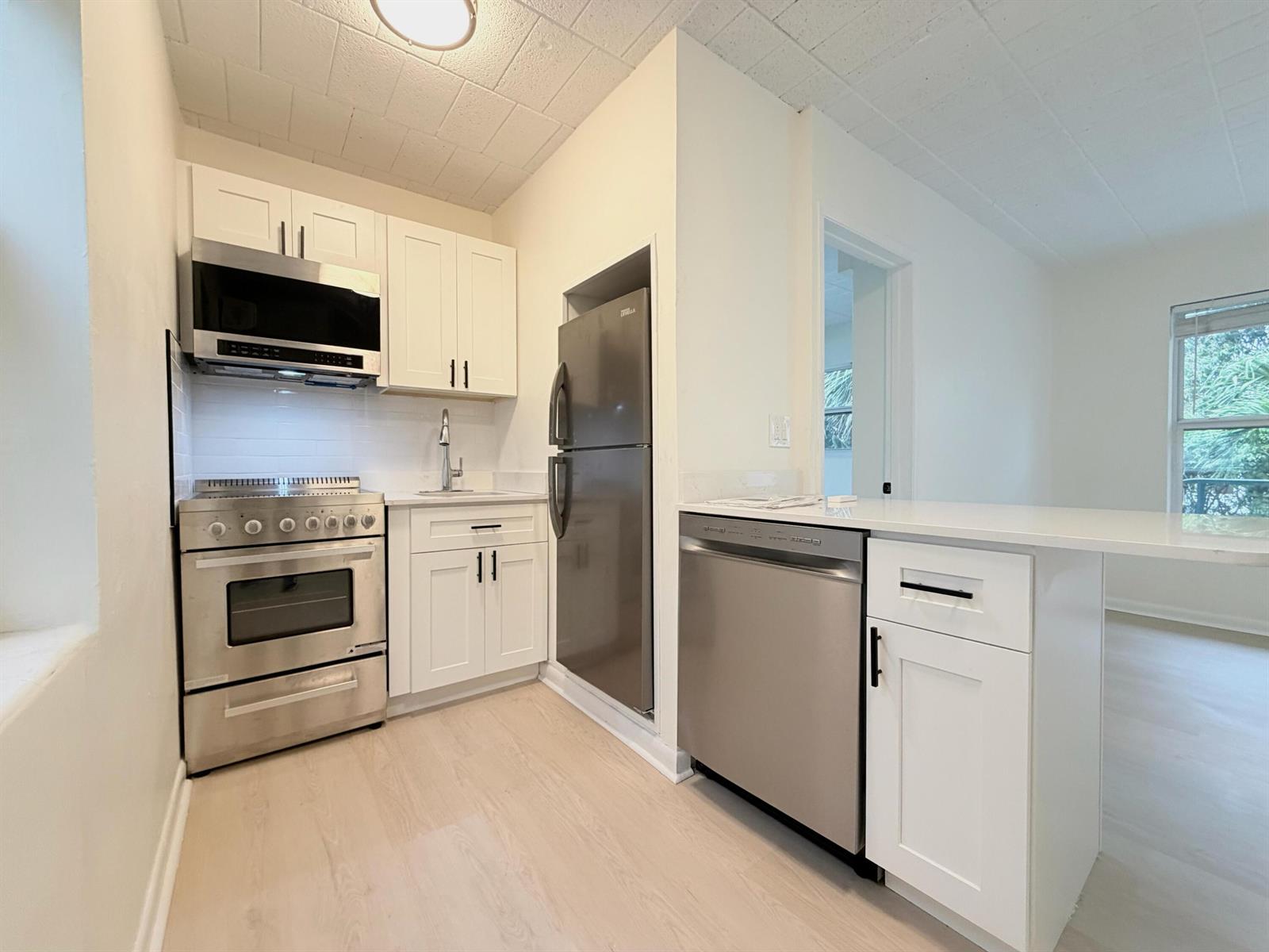 A kitchen features white cabinets, stainless steel appliances, and light wood-look flooring — 1713 Florida Avenue Unit B4, West Palm Beach FL 33401, WEST PALM BEACH, FL