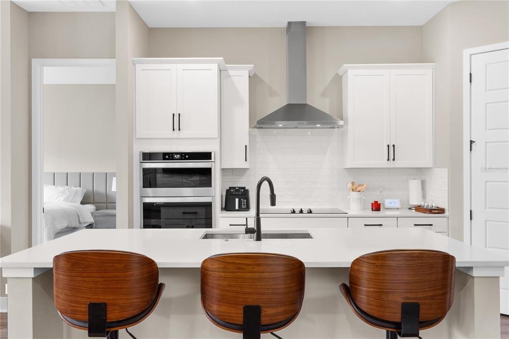 A modern kitchen features white cabinets, stainless steel appliances, a quartz island, and three barstools — 16055 SILVER BROOK WAY, WINTER GARDEN, FL