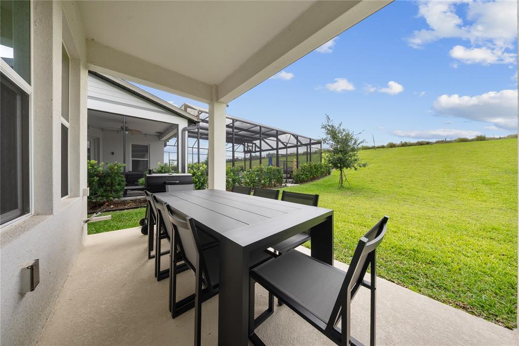 A covered patio features a black dining set overlooking a grassy backyard and neighboring pool cage — 16055 SILVER BROOK WAY, WINTER GARDEN, FL