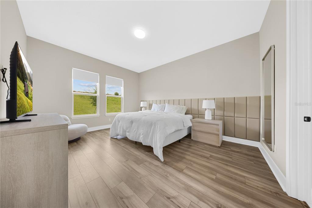A bedroom features light wood-look flooring, a tufted headboard wall, and two windows with views — 16055 SILVER BROOK WAY, WINTER GARDEN, FL