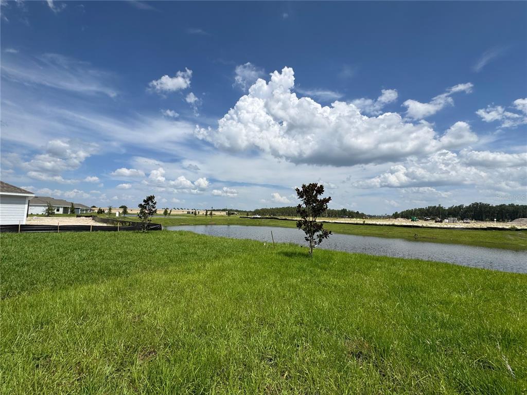 A grassy lot overlooks a small pond with a house under construction in the distance — 5596 MORANT BAY PATH, KISSIMMEE, FL