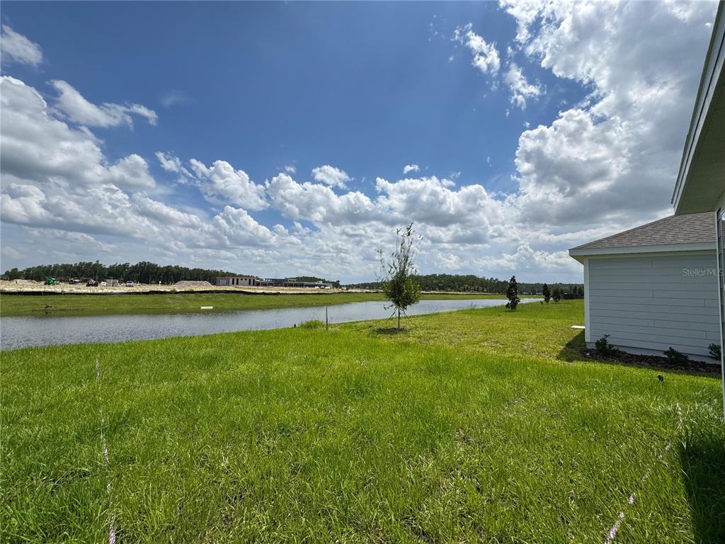 A grassy backyard overlooks a pond with a house exterior visible on the right — 5596 MORANT BAY PATH, KISSIMMEE, FL