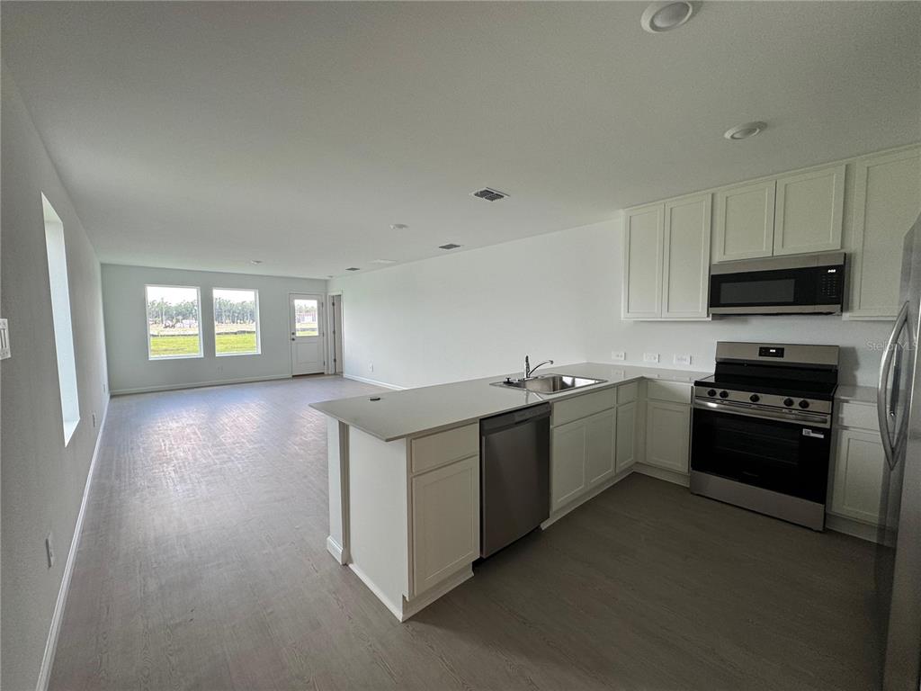 A kitchen with white cabinets and stainless steel appliances opens into a large living area — 5596 MORANT BAY PATH, KISSIMMEE, FL