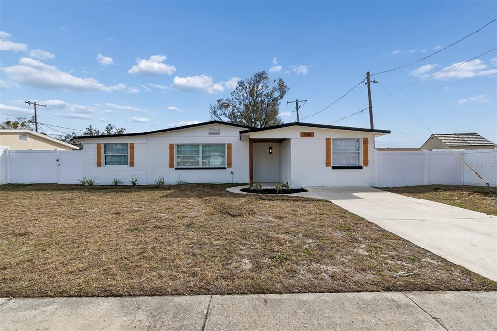 A white single-story house with a concrete driveway and a fenced yard under a blue sky — 7910 W POWHATAN AVENUE, TAMPA, FL