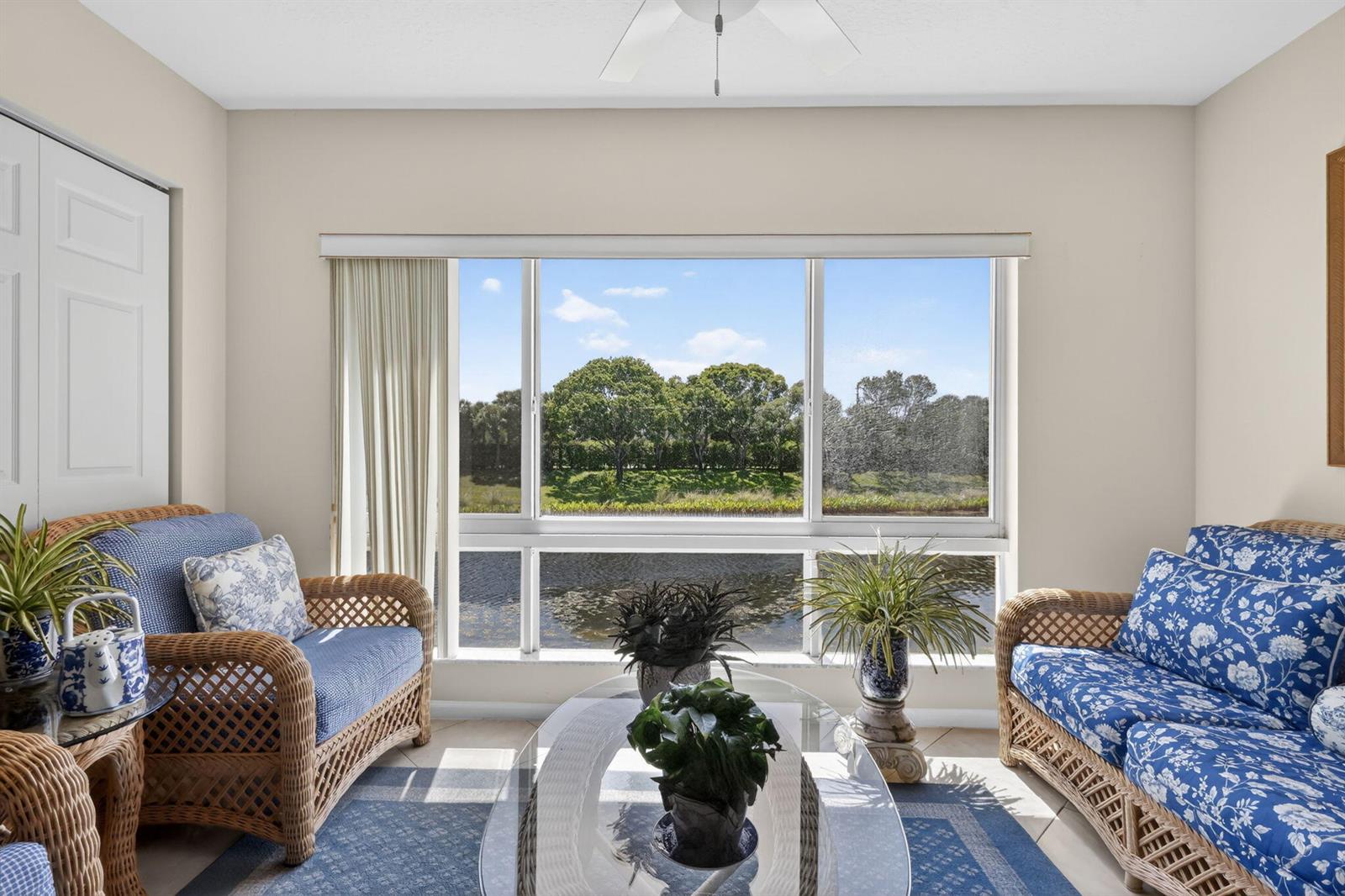 A sunroom with wicker furniture and a large window overlooking a pond and trees — 5906 Crystal Shores Drive # 208, Boynton Beach FL 33437, BOYNTON BEACH, FL