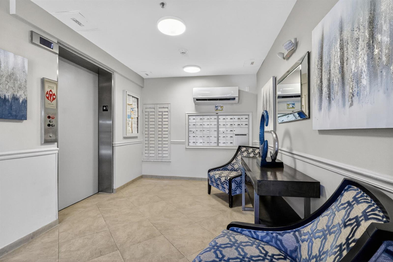 This apartment building lobby features an elevator, mailboxes, two patterned chairs, and a console table — 5906 Crystal Shores Drive # 208, Boynton Beach FL 33437, BOYNTON BEACH, FL