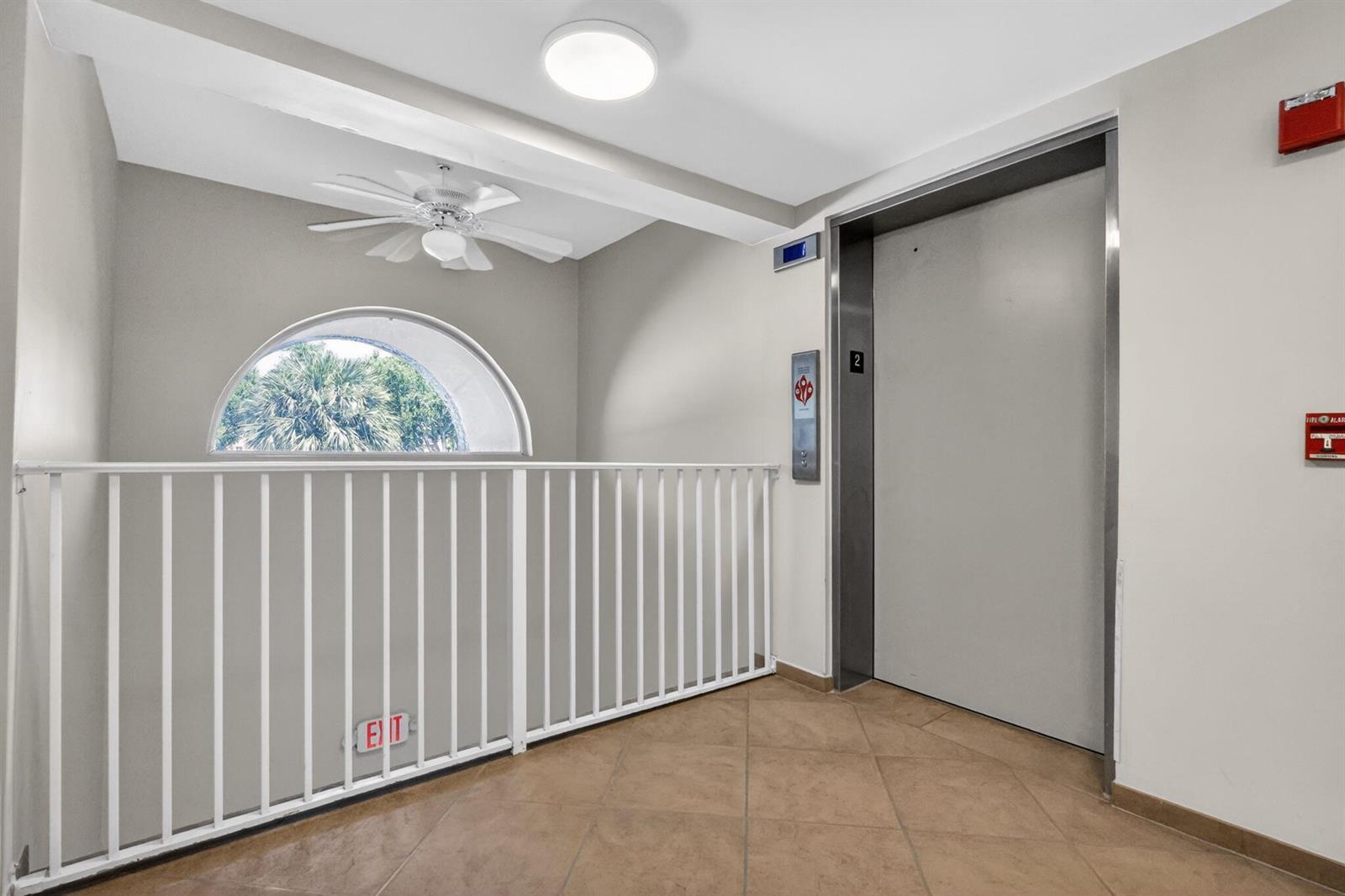 An elevator lobby features beige tile flooring, a white ceiling fan, and an arched window — 5906 Crystal Shores Drive # 208, Boynton Beach FL 33437, BOYNTON BEACH, FL