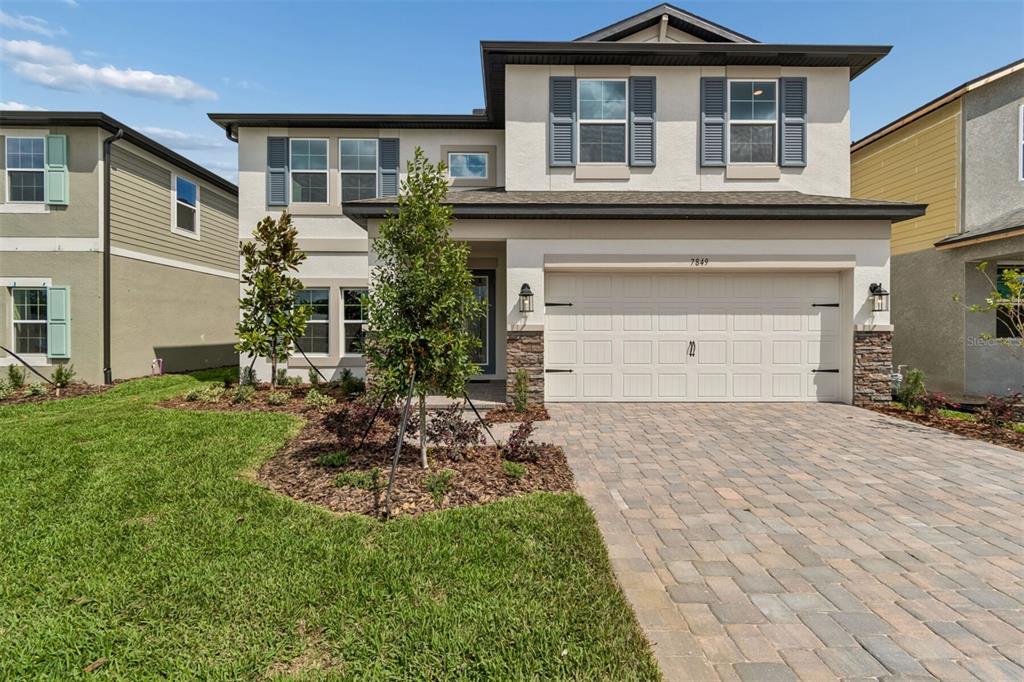 A two-story suburban house features a paved driveway, a two-car garage, and light-colored stucco siding — 7849 PAINTED SKY PLACE, LAND O LAKES, FL