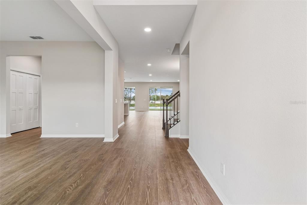An interior view shows a hallway with wood-look flooring leading toward a bright living area — 7849 PAINTED SKY PLACE, LAND O LAKES, FL