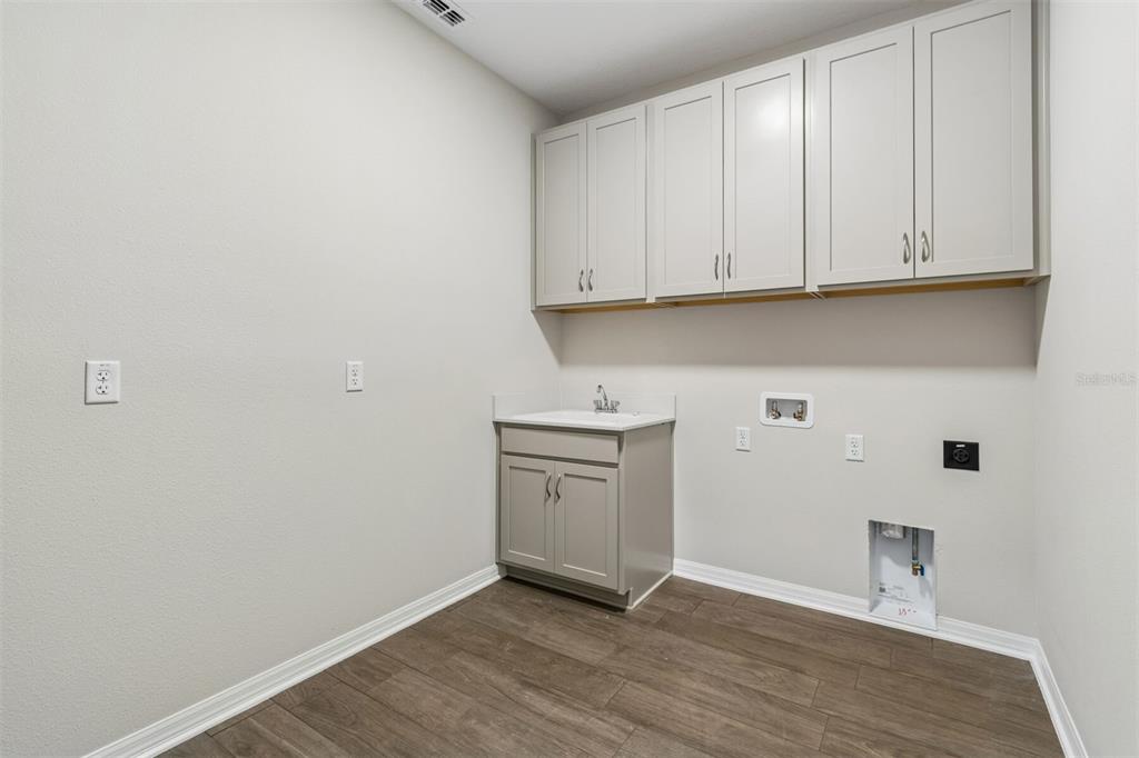 A laundry room features light gray cabinets, a utility sink, and wood-look flooring — 7849 PAINTED SKY PLACE, LAND O LAKES, FL