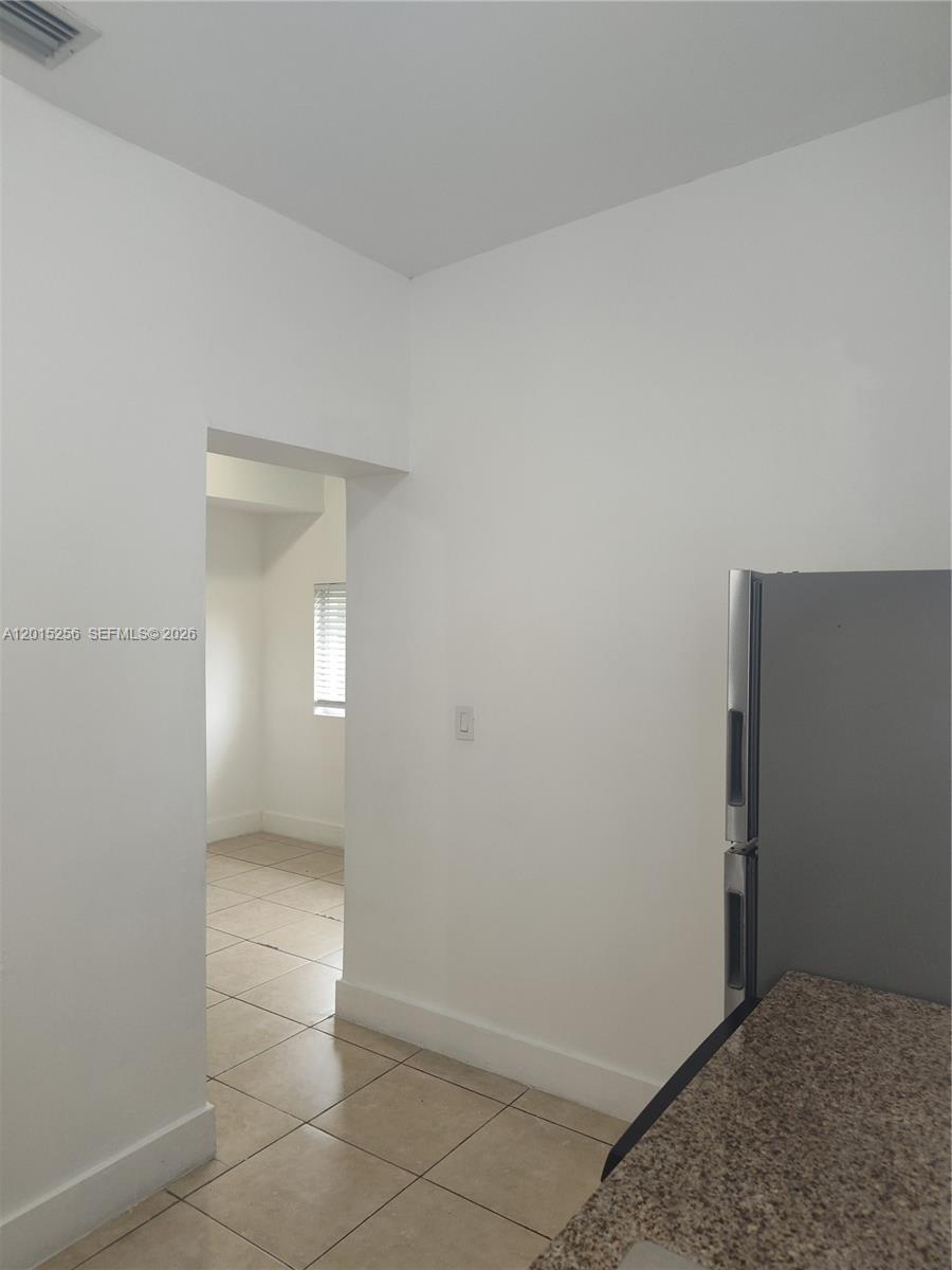 A kitchen with a granite countertop and stainless steel refrigerator leads into an adjacent room — 8028 NW 5th Ct Rear, Miami FL 33150, MIAMI, FL