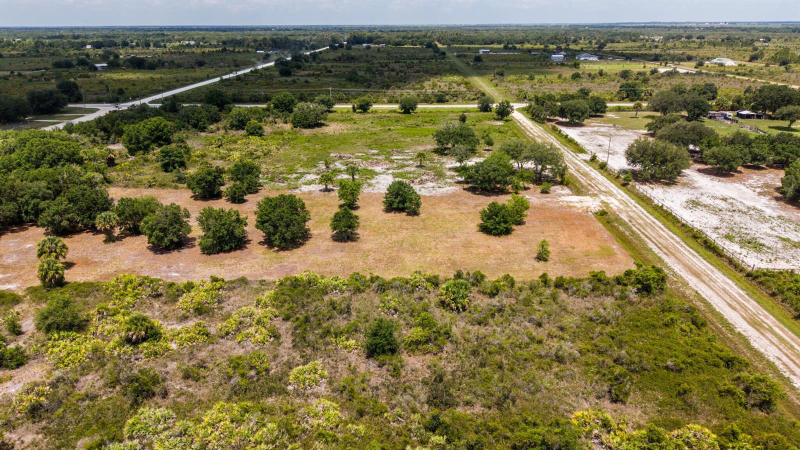 An aerial view shows a large, grassy, partially wooded vacant lot bordered by a dirt road — 19371 NW 254th Street, Okeechobee FL 34972, OKEECHOBEE, FL